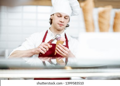 Young Salesman In Apron And Hat Making Ice Cream With Waffle Cone At The Modern Pastry Shop