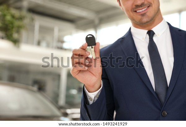 Young salesman with car key in modern dealership,\
focus on hand