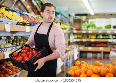 Young salesman holding box of tomatoes during work on the supermarket - Shutterstock ID 1836554875