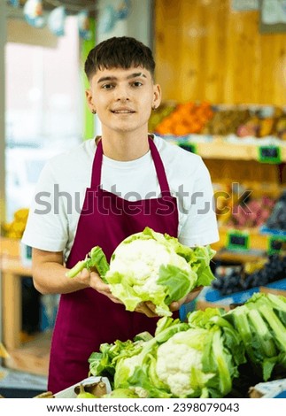 Young salesman proposing cauliflower, offering fresh vegetables in supermarket
