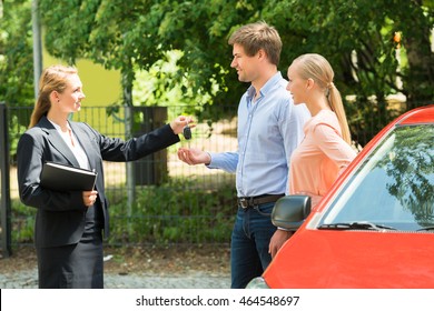 Young Saleswoman Giving Car Key To Happy Couple