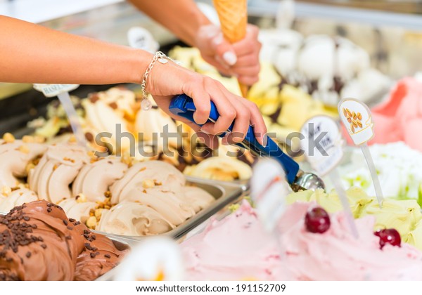 Young saleswoman in an ice cream parlor takes a\
scoop of ice cream