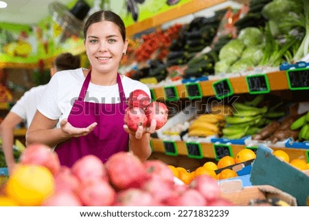 Young saleswoman proposing pomegranate, offering fresh fruits in supermarket