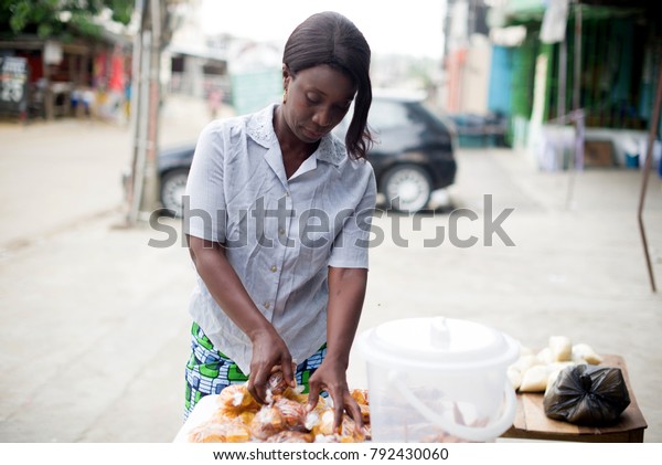 young saleswoman standing\
in front of her sales table and placing packets of chips on the\
table outside