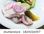 Young salted fish called soused or matjes herring with sour cream, gherkin and red onions, served with salad on a white plate, selected focus, narrow depth of field