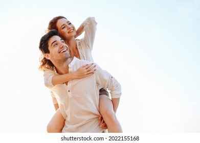 Joven feliz feliz feliz y encantado pareja sonriente dos amigos hombre de familia con ropa casual novio le da paseo en piggyback a la alegre novia se sienta en la espalda mira a un lado con fondo blanco claro