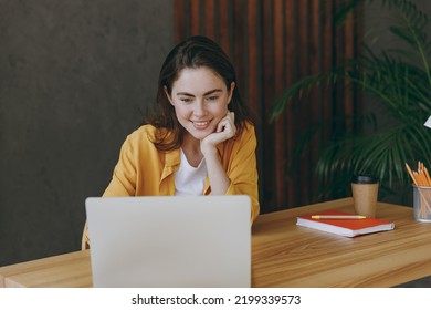 Young satisfied fun happy successful employee business woman 20s she wearing casual yellow shirt hold use laptop pc computer sit work at wooden office desk with pc laptop. Achievement career concept - Shutterstock ID 2199339573