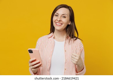 Young Satisfied Fun Happy Woman She 30s Wears Striped Shirt White T-shirt Hold In Hand Use Mobile Cell Phone Chatting Onlie Browsing Internet Show Thumb Up Isolated On Plain Yellow Background Studio.