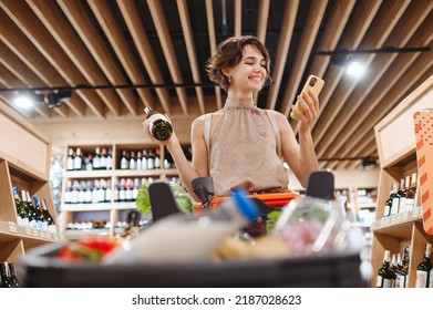 Young satisfied fun woman in casual clothes shopping at supermaket store with grocery cart hold white wine alcohol hold bottle talk speak mobile phone inside hypermarket Purchasing gastronomy concept. - Powered by Shutterstock