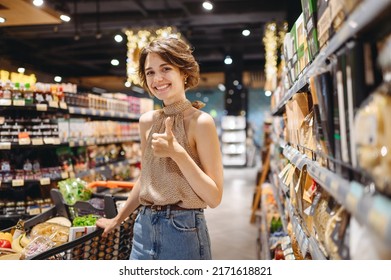 Young satisfied happy fun woman in casual clothes shopping at supermaket store buy choosing pasta with grocery cart show thumb up gesture inside hypermarket. People purchasing gastronomy food concept. - Powered by Shutterstock