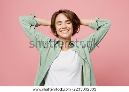 Young satisfied happy fun woman 20s she wear green shirt white t-shirt hold hands behind neck close eyes smiling isolated on plain pastel light pink background studio portrait People lifestyle concept