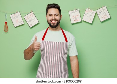 Young Satisfied Happy Smiling Male Chef Confectioner Baker Man 20s In Striped Apron Showing Thumb Up Like Gesture Isolated On Plain Pastel Light Green Background Studio Portrait. Cooking Food Concept