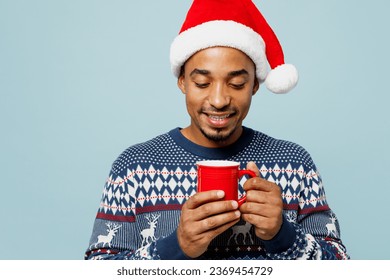 Young satisfied smiling man wear knitted sweater Santa hat posing hold in hand cup with coffee or tea isolated on plain pastel blue background Happy New Year 2024 celebration Christmas holiday concept - Powered by Shutterstock