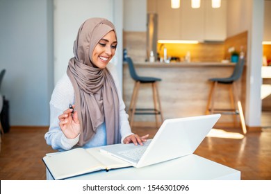 Young Saudi Business Woman Working In At Home, Pointing On Laptop, Copy Space. Muslim Female Working With Computer In The Room , Writing Paper. Young Muslim Woman Using Laptop