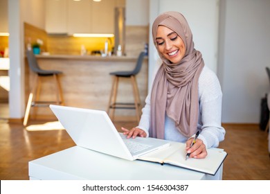 Young saudi business woman working in at home, pointing on laptop, copy space. Muslim female working with computer in the room , writing paper. Young muslim woman using laptop