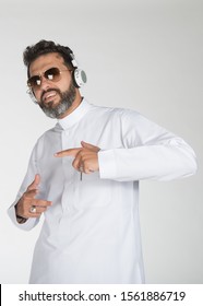 Young Saudi Man Wearing White Thobe Putting The Headphone On And Dancing On  Isolated White Background.