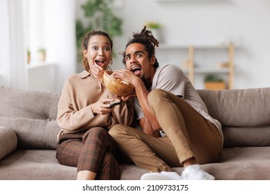 Young scared african american family couple screaming while watching horror movie with popcorn together at home, selective focus. Emotional reactions to scary film. Leisure activities in relationships