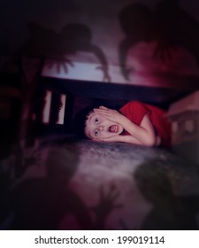 A Young Scared Boy Is Hiding Under A Bed Looking At Black Scary Monster Ghosts In Fear For A Bedtime Or Evil Concept.