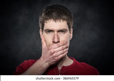 Young Scared Man Hand Covering Mouth Over Dark Background.