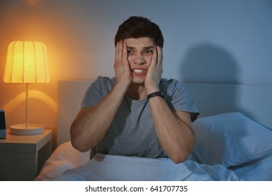 Young Scared Man Sitting On Bed At Home