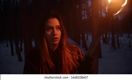 Young Scared Woman With Long Hair Walking In The Night Winter Forest Holding A Handmade Torch