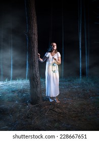 Young Scared Woman Walking In Foggy Night Forest With Lantern