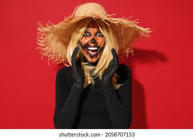 Young scary woman with Halloween makeup mask wearing straw hat black scarecrow costume scream hot news with hands near mouth isolated on plain red background studio. Celebration holiday party concept