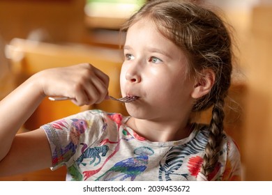 Young School Age Girl, Little Child Eating Her Meal, Holding A Fork In Mouth, Indoors Portrait, Face Closeup, Shallow Depth Of Field. Children, Childhood Nutrition, Appetite, Healthy Lifestyle Concept