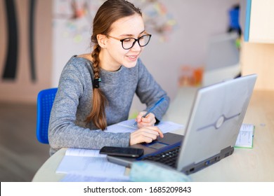 Young School Girl Left-handed Working At Home In Her Room With A Laptop And Class Notes Studying In A Virtual Class. Distance Education And E-learning, Online Learning Concept During Quarantine