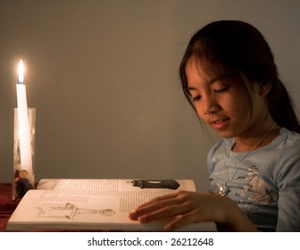 Young School Girl Reading A Book By Candle Light.