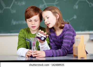 Young school kids doing a chemistry experiment with the little boy holding the flask steady while the little girl pours over a colorful liquid - Powered by Shutterstock