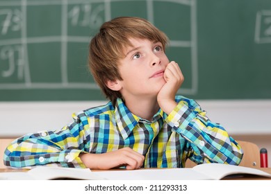 Young Schoolboy Daydreaming In Class As He Sits At His Desk In Front Of The Blackboard Staring Thoughtfully Up Into The Air Wishing He Were Playing Outdoors