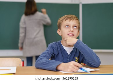 Young Schoolboy Hoping For An Answer To A Question In His Class Work Sitting Staring Up Into The Air With His Hand To His Chin As He Sits At His Desk