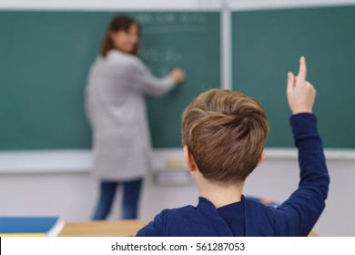 Young Schoolboy Putting Up His Hand In Class To Answer A Question For His Teacher, View From Behind His Head