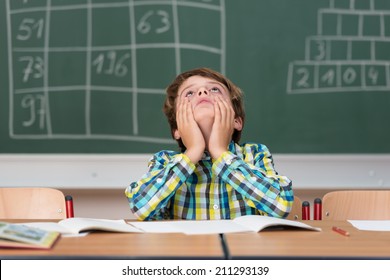 Young Schoolboy Searching For Answers Sitting At His Desk In The Classroom Staring Up Into The Air With A Thoughtful Expression