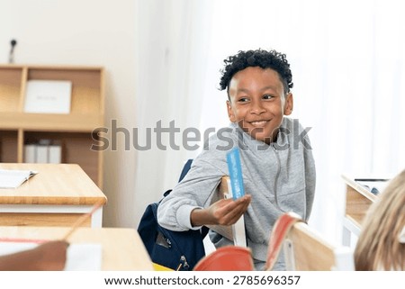 Young schoolboy smiles while sharing blue ruler with classmate during elementary classroom routine, building friendship, participation, motivation, teamwork, confidence on opening day lesson.