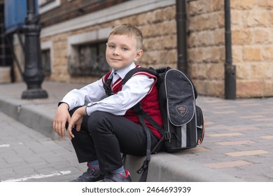 A young schoolboy in uniform with a backpack patiently waiting for classes near the school. - Powered by Shutterstock