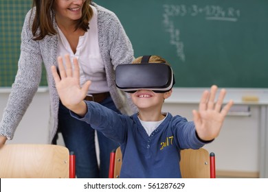 Young schoolboy wearing a VR headset experiencing virtual reality for the first time watched by a smiling teacher - Powered by Shutterstock