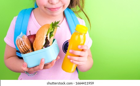 Young Schoolgirl With Lunch Box On A Green Background. Little Girl With A School Backpack And A Set Of Food For A Snack. Free Space For Text