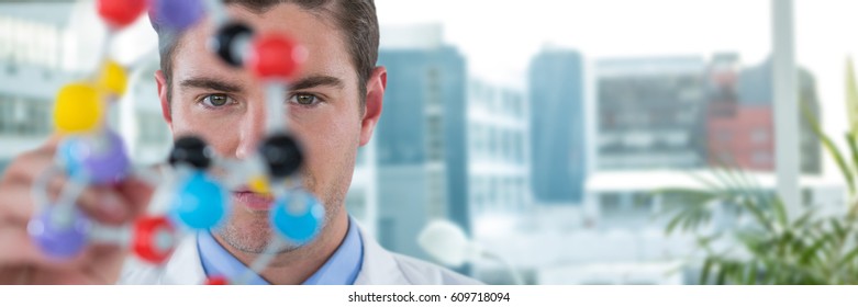 Young scientist experimenting molecule structure against laptop on desk by glass window in office