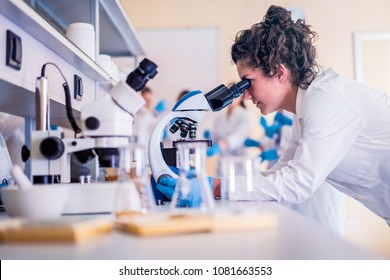 Young scientist looking through a microscope in a laboratory doing research - Powered by Shutterstock