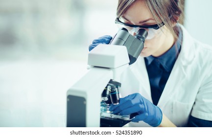 Young scientist looking through a microscope in a laboratory. Young scientist doing some research. - Shutterstock ID 524351890
