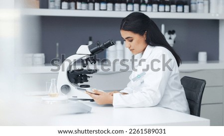 Young scientist using a digital tablet and microscope in a lab. Female pathologist analyzing medical samples while doing experiments to develop a cure. Microbiologist conducting forensic research