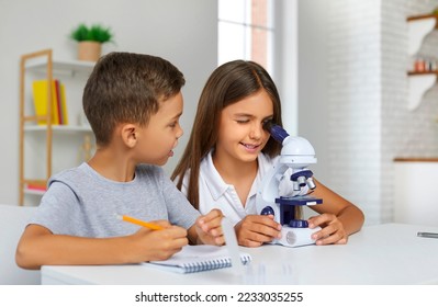 Young scientists. Little brother and sister together doing some experiments with microscope at home. Preschool boy and girl conduct science experiments and take notes while sitting at table in room. - Powered by Shutterstock