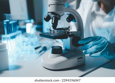 Young scientists in sterile clothing and safety goggles sitting at table conducting research investigations in a medical laboratory using a microscope, Serious concentrated female microbiologist. - Powered by Shutterstock