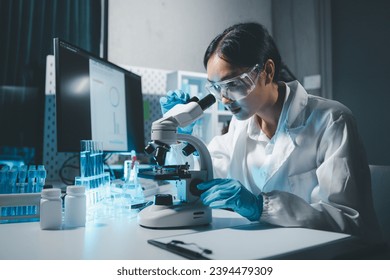 Young scientists in sterile clothing and safety goggles sitting at table conducting research investigations in a medical laboratory using a microscope, Serious concentrated female microbiologist. - Powered by Shutterstock