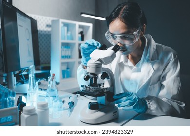 Young scientists in sterile clothing and safety goggles sitting at table conducting research investigations in a medical laboratory using a microscope, Serious concentrated female microbiologist. - Powered by Shutterstock