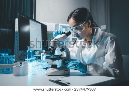 Young scientists in sterile clothing and safety goggles sitting at table conducting research investigations in a medical laboratory using a microscope, Serious concentrated female microbiologist.