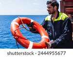 Young seafarer with lifebuoy on the cargo ship - he is throwing lifebuoy overboard to help to the person fallen into the sea.