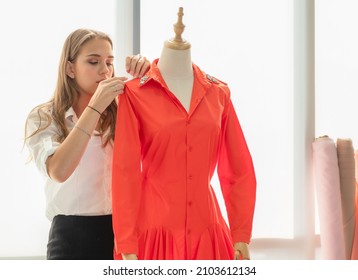 Young seamstress working in boutique showroom checking completeness of red dress on mannequin. Beautiful stylish fashion designer small business owner handmade creative fashionable clothes in studio. - Powered by Shutterstock